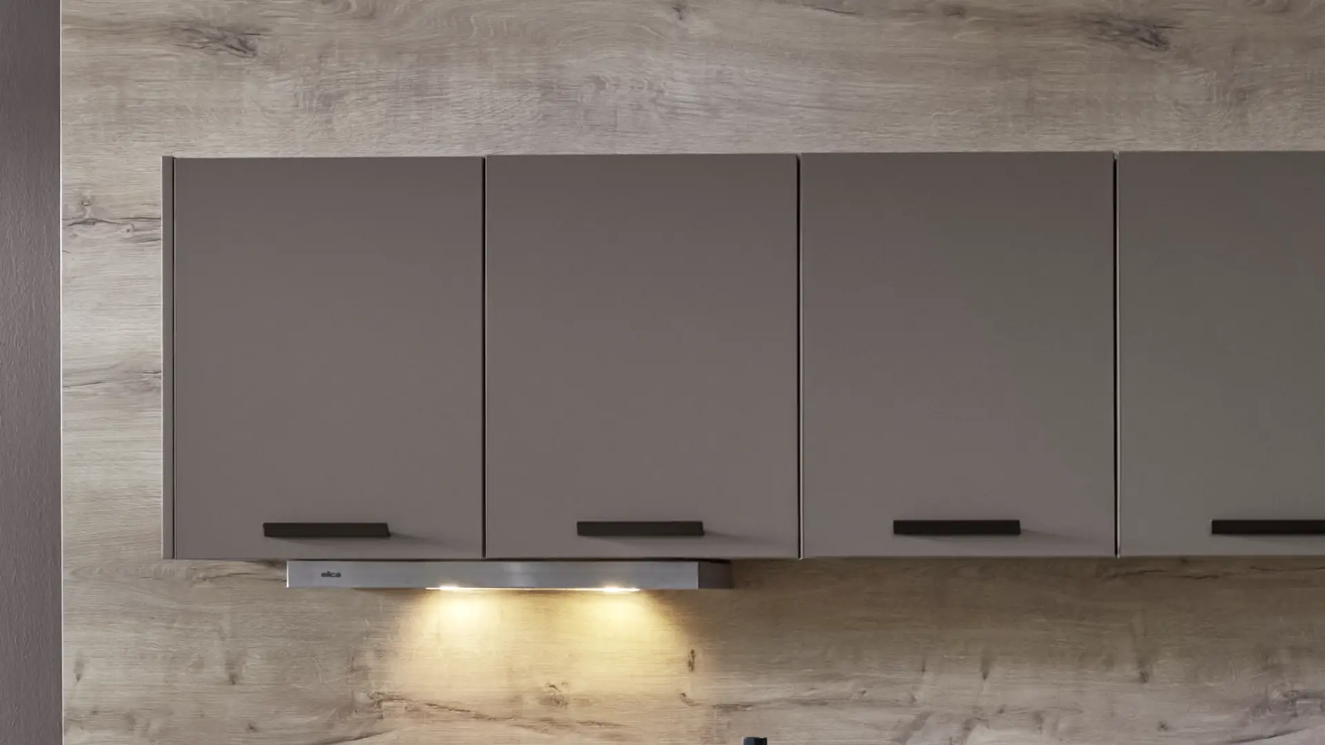 Moderne Küchenschränke in mattem Grau mit schwarzen Griffen, montiert auf einer Holzrückwand, mit integrierter Beleuchtung unter dem Schrank.
