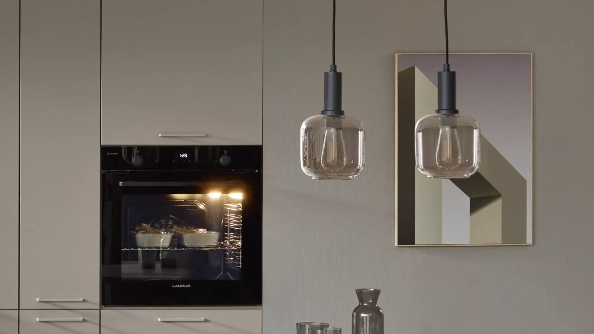Moderne Einbauküche mit einem schwarzen Ofen, der eingeschaltet ist und zwei Backformen mit Essen zeigt, zwei hängenden Glaslampen und einem geometrischen Wandbild.