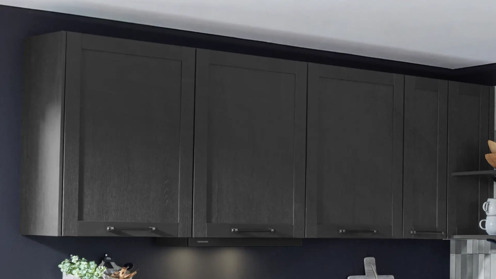 Schwarze Hängeschränke einer modernen Küche vor einer dunkelblauen Wand mit integriertem Dunstabzug und Beleuchtung darunter.