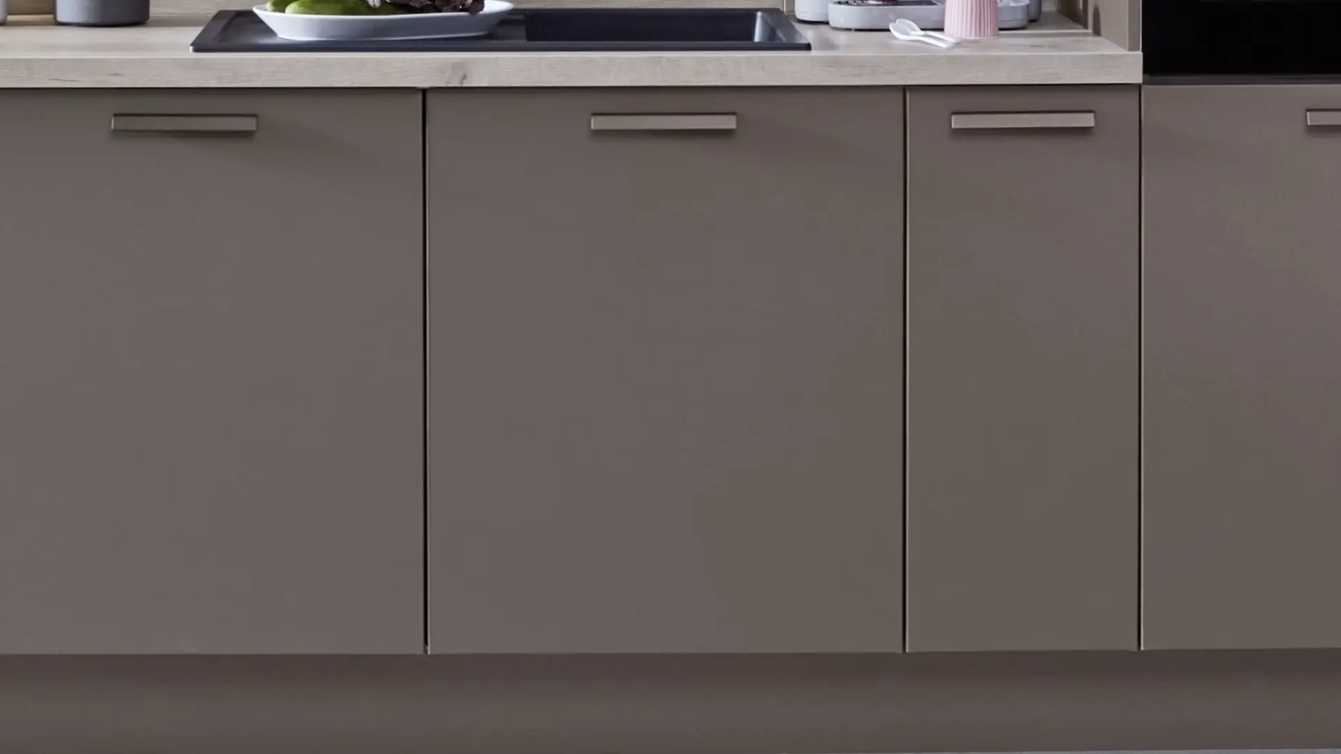 Moderne Küche mit grauen Unterbau-Schränken und Arbeitsplatte, darauf Gemüseschale und Spüle.