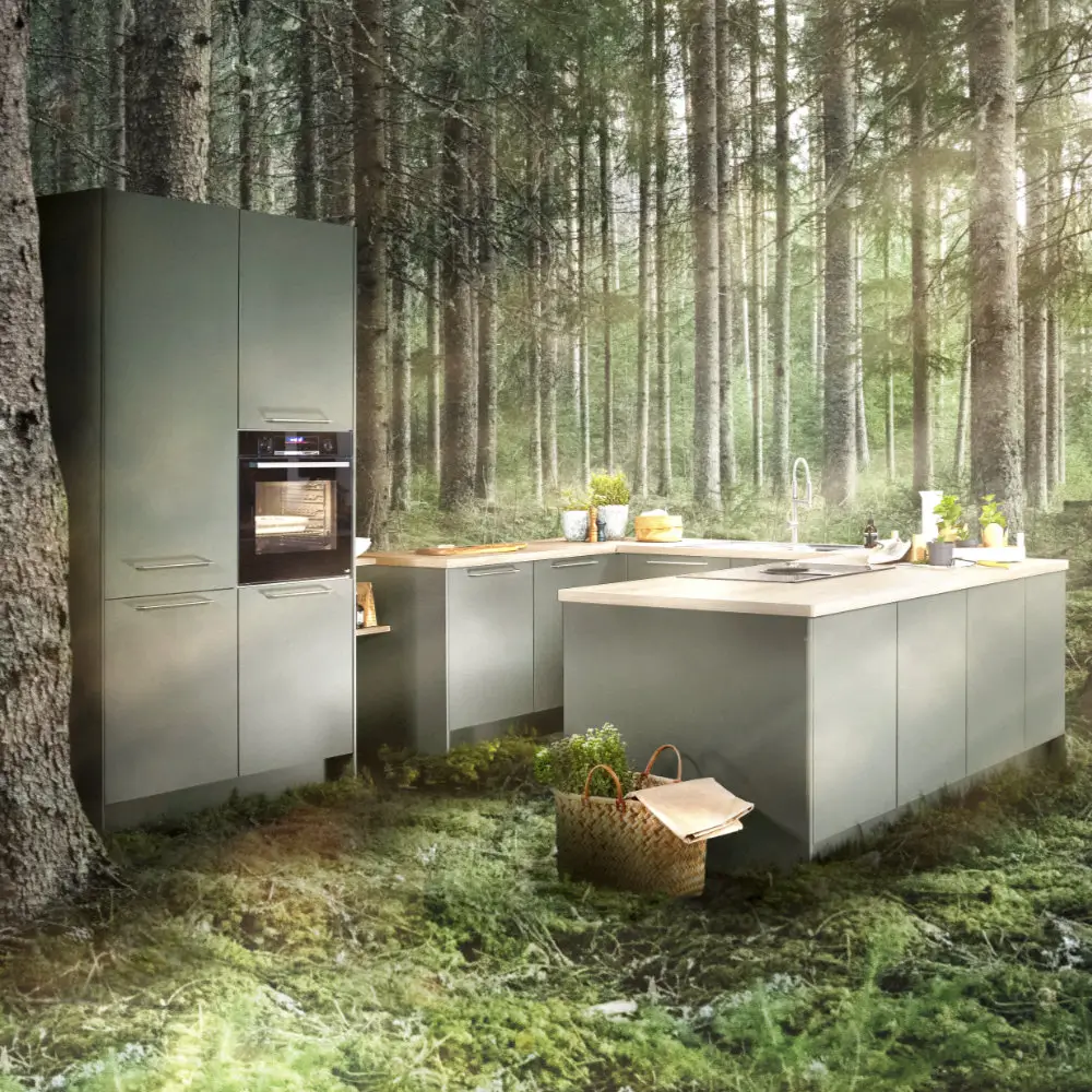 Moderne, graue Küchenzeile mit integriertem Backofen und Kochinsel, platziert auf moosbedecktem Waldboden umgeben von hohen Bäumen im Wald.