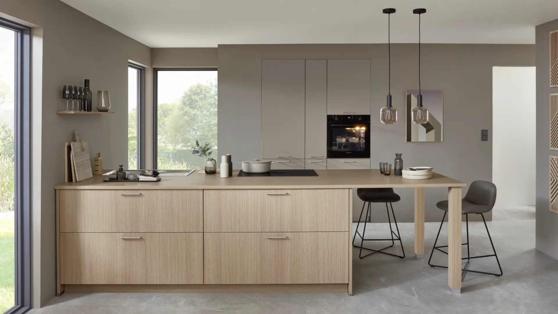 Moderne Küche mit Holzinsel, integrierter Kochplatte und Backofen, zwei Hockern, grauen Wänden und großen Fenstern mit Blick ins Grüne.